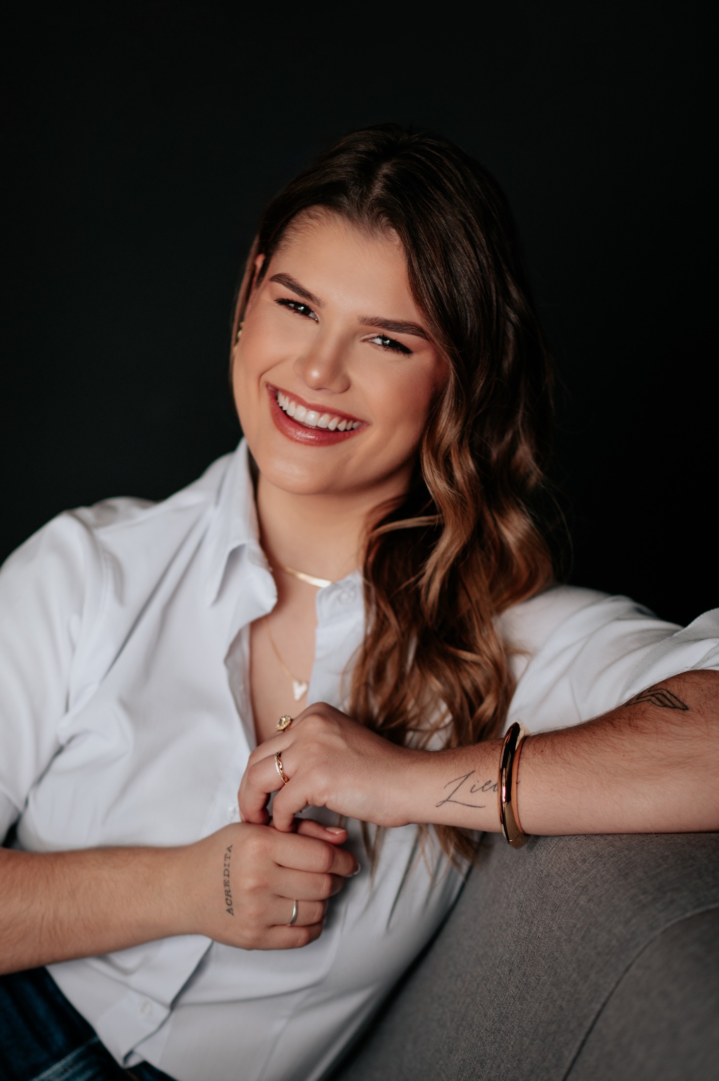 Maria sorrindo, de camisa branca, em retrato sobre fundo escuro